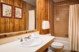 Cozy bathroom with wood paneling, a light-colored countertop, white towels, and a shower curtain, featuring floral artwork on the walls.