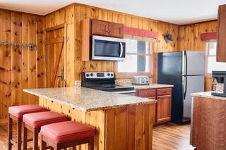 A cozy kitchen features wood paneling, granite countertops, modern appliances, and red bar stools, creating a warm and inviting atmosphere.