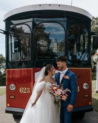 A happy couple shares a moment outside a vintage trolley, adorned with flowers, celebrating their wedding with joy and love.