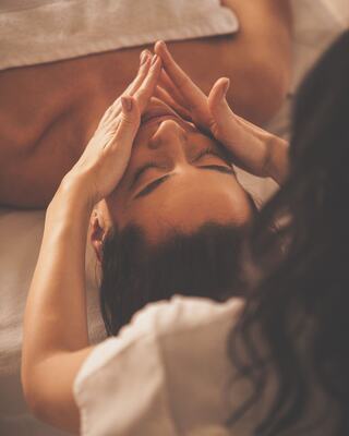 A person receives a relaxing facial massage, eyes closed, as hands gently apply pressure to their face in a serene setting.