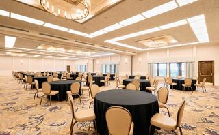 A spacious banquet hall features numerous round tables with black linens and elegant lighting, providing a sophisticated setting for events.