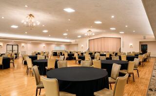 An elegant event space with wooden floors, round tables covered in black cloth, and tasteful lighting, ready for gatherings or celebrations.