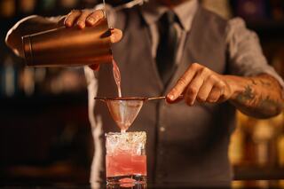 A bartender skillfully strains a vibrant pink cocktail into a glass, showcasing a blend of elegance and mixology expertise.