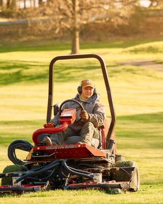A person operates a riding lawn mower on a lush green lawn, enjoying a sunny day with trees in the background.