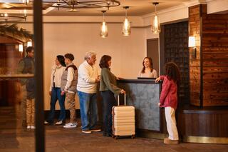 A family checks in at a hotel reception, chatting with the front desk staff. Luggage is present, creating a welcoming atmosphere.