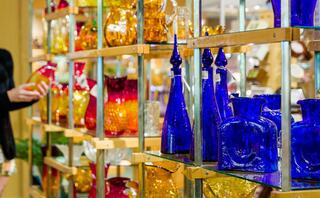 A vibrant display of colorful glass vases and bottles in various shapes, highlighted by rich blues, reds, and yellows, catches the eye.