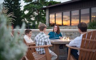 A woman engages warmly with three boys around a fire pit as the sun sets, creating a cozy and inviting atmosphere.