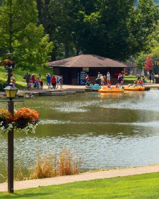 A vibrant park scene by a calm lake showcases families enjoying activities, colorful kayaks, and lush greenery under sunny skies.