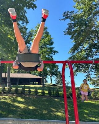 A child swings upside down from a swing set, while another child swings nearby, enjoying a sunny day at the park.