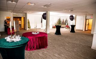 A spacious, elegantly decorated event space features round tables, festive greenery, and soft lighting, creating a welcoming atmosphere.