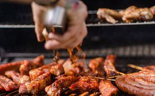 Juicy, grilled meats sizzle on a barbecue, with a hand sprinkling seasoning over the tantalizing spread of ribs and sausages.