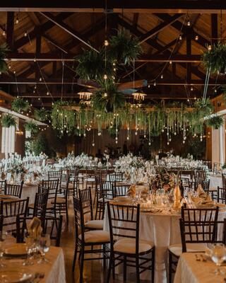 An elegant venue features beautifully set tables with floral decor, rustic wooden beams, and hanging greenery, creating a romantic ambiance.