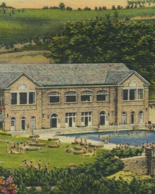 A vintage scene featuring a large brick building by a pool, with people enjoying leisure time in a lush, green landscape.