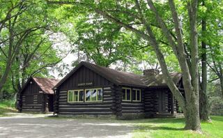 A charming log cabin nestled among lush green trees, featuring large windows and rustic architecture, suggesting a serene retreat.