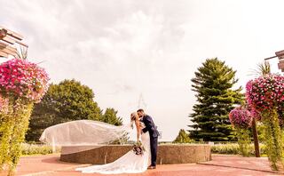 A couple shares a romantic kiss in a picturesque garden, surrounded by vibrant flowers and lush greenery, capturing a beautiful wedding moment.