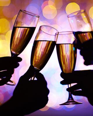 Four hands holding champagne flutes toast against a backdrop of colorful bokeh lights, creating a festive and celebratory atmosphere.
