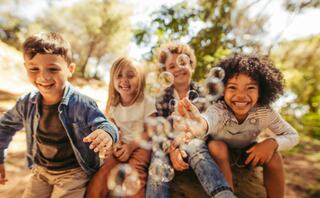 Four joyful children play together outdoors, laughing and reaching out to catch floating bubbles amidst a natural, sunny setting.