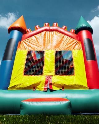 A colorful bouncy castle with towers, a bright yellow entrance, and mesh windows sits on green grass under a blue sky.