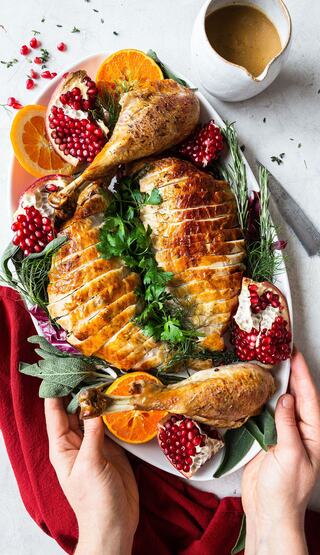 A beautifully arranged platter features golden roasted chicken, garnished with herbs, pomegranate, and oranges, showcasing vibrant colors and textures.