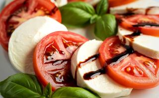 Slices of fresh mozzarella and ripe tomatoes, drizzled with balsamic glaze, garnished with vibrant basil leaves. A colorful, appetizing dish.