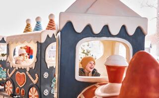 A joyful child wearing a tan hat smiles while peeking out from a whimsical train made of ice cream and candy decorations.