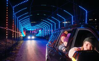 A car drives through a dazzling, colorful light tunnel at night, with excited passengers enjoying the festive atmosphere.