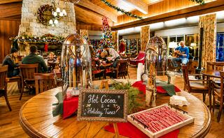 A cozy festive gathering features hot cocoa, candy canes, and holiday decorations, with guests enjoying music by a warmly lit fireplace.
