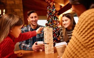 A family enjoys a holiday gathering, playing a game of Jenga while sipping warm drinks, surrounded by festive decorations.