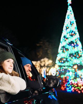 A couple enjoys the festive atmosphere, gazing at a brightly lit Christmas tree while sitting in their car on a cozy winter night.