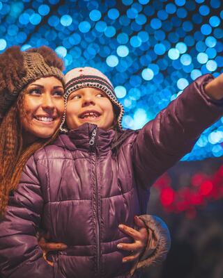 A joyful woman and child smile broadly, surrounded by vibrant, colorful lights, as the child points excitedly at something off-screen.