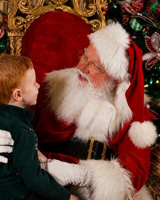 A cheerful Santa in a red suit joyfully interacts with a young boy, surrounded by festive decorations and a Christmas tree.