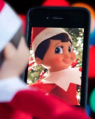 A cheerful elf doll is captured on a smartphone screen, surrounded by festive decorations in soft, colorful bokeh.