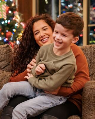 A joyful moment captured between a woman and a boy, filled with laughter, holiday decorations twinkling in the background.