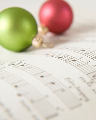 Green and red ornaments sit on sheet music, evoking a festive atmosphere centered around holiday tunes and melodies.