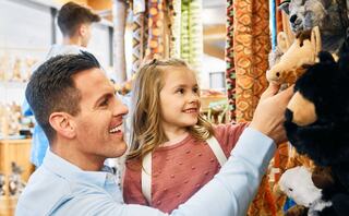 A man and a young girl happily explore a shop filled with stuffed animals, sharing a joyful moment together.