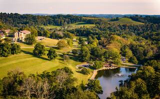 A picturesque landscape features rolling hills, lush greenery, and a tranquil pond, surrounded by trees and a residential area.