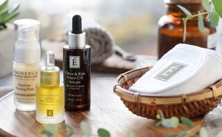 Three skincare products are arranged on a wooden surface, accompanied by a cotton pad in a woven basket, all set in a natural, calming environment.