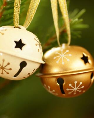 Two decorative bells, one golden and the other cream, hang from a green tree branch, adorned with snowflake patterns and star designs.