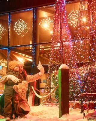 A woman and a child pose joyfully in a winter setting, surrounded by colorful lights and festive decorations, capturing a cheerful moment together.
