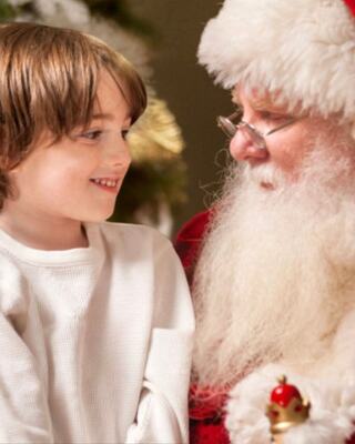 A smiling child in a white shirt joyfully interacts with a cheerful Santa Claus, sharing a magical holiday moment.