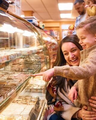 A woman and a young boy joyfully point at treats in a bakery, sharing a moment of excitement and delight amidst colorful confections.