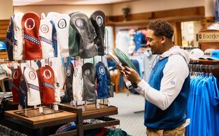 A man examines golf gloves on display in a retail store, surrounded by various apparel and accessories.