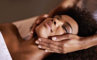 A woman relaxes with her eyes closed, enjoying a soothing massage as a gentle hand supports her neck and face.