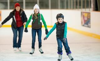 A joyful trio skates on ice, with a smiling girl in front showcasing her skills while her family encourages her from behind.
