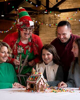 A cheerful group gathers to decorate a colorful gingerbread house, enjoying a festive, joyful atmosphere filled with holiday spirit.