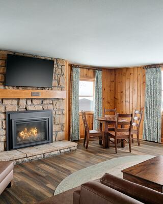 Cozy interior with a stone fireplace, wooden paneling, a dining table, and plush seating, evoking a warm, inviting atmosphere.