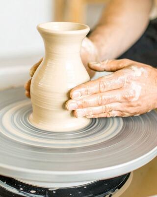 A pair of hands expertly shapes a beige clay vase on a spinning pottery wheel, showcasing the artistry of ceramics.