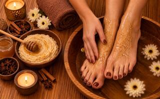 Relaxing spa scene featuring beautifully manicured feet in a bowl of warm water, surrounded by candles, flowers, honey, and natural scrubs.