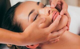A serene woman enjoys a facial massage, with gentle hands applying soothing techniques to her relaxed face.