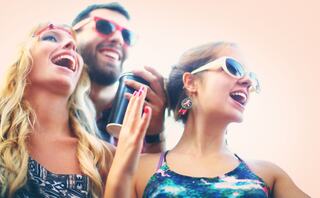 Three friends joyfully sing together, wearing sunglasses and smiling, capturing a carefree moment of fun and friendship.